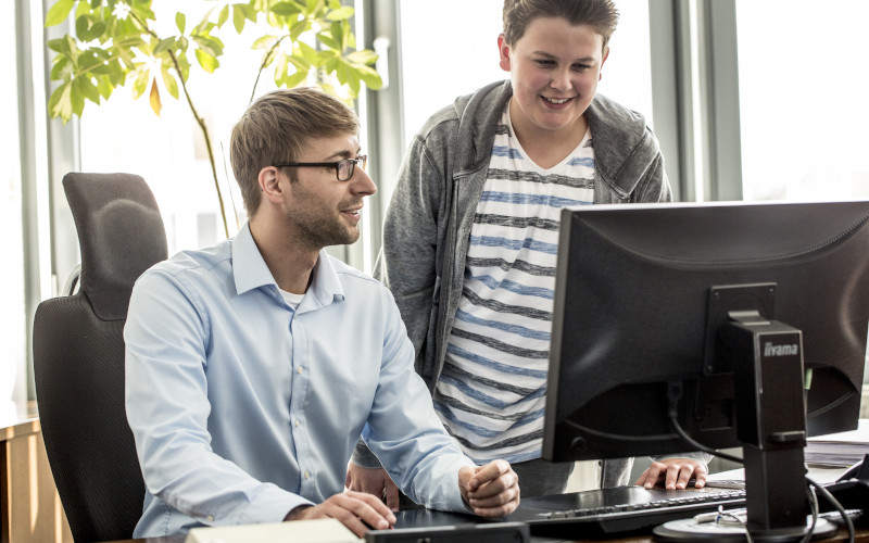 Junge lässt sich von Büromitarbeiter etwas am Computer erklären